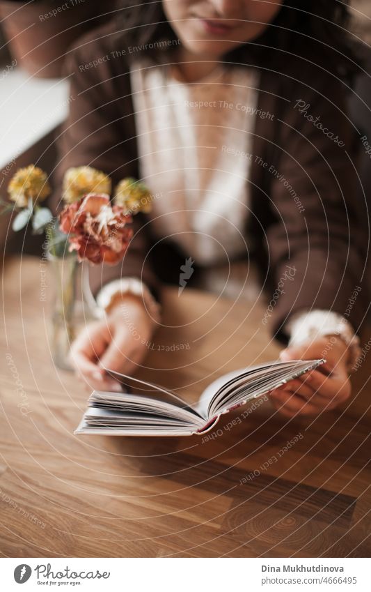 Frau liest ein Buch im Café sitzt am Holztisch mit Blumen in einer Vase. Romantisches Date mit einem Buch. Brown Vintage neutrale Farbe Hintergrund. Literatur & Bibliothek, Buch-Liebhaber verbringen Freizeit.