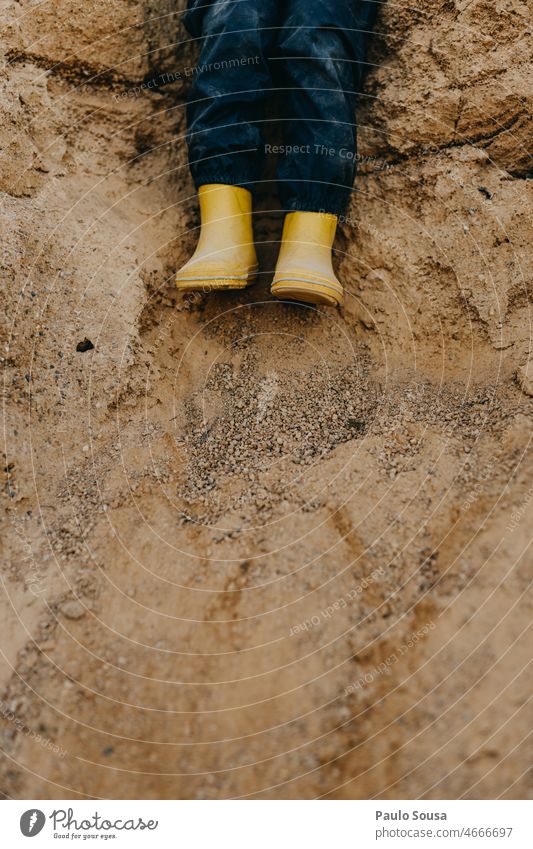 Kind mit gelben Gummistiefeln auf Sand Nahaufnahme dreckig Schuhe Beine Farbfoto Stiefel Außenaufnahme Fuß schlechtes Wetter Spielen Kindheit Textfreiraum unten