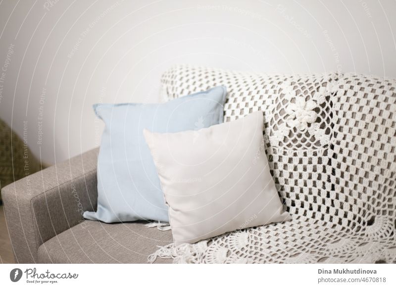 Kissen auf einer Couch in der Nähe von weißen Wand. Hellblaue und graue Kissen und gestrickte Decke auf einem beigen Sofa in skandinavischen minimalistischen Stil Wohnung Interieur. Home Decor mit Kopie Raum oben.
