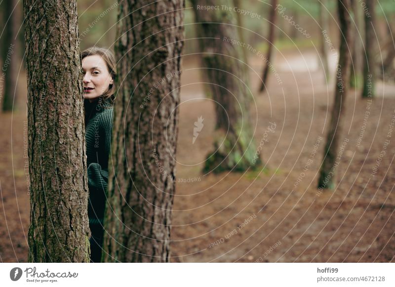ein Frau schaut, verdeckt von Bäumen, selbstbewusst in die Kamera Blick in die Kamera Porträt besinnlich Auge Naturerlebnis Darstellerin Baumstamm