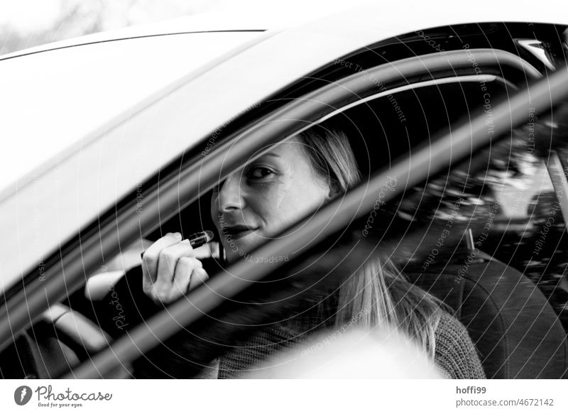 eine Frau sitzt im Auto, schminkt sich und blickt durch die geöffnete Tür in die Kamera im auto Schminken schminken Lippenstift Gesicht Junge Frau