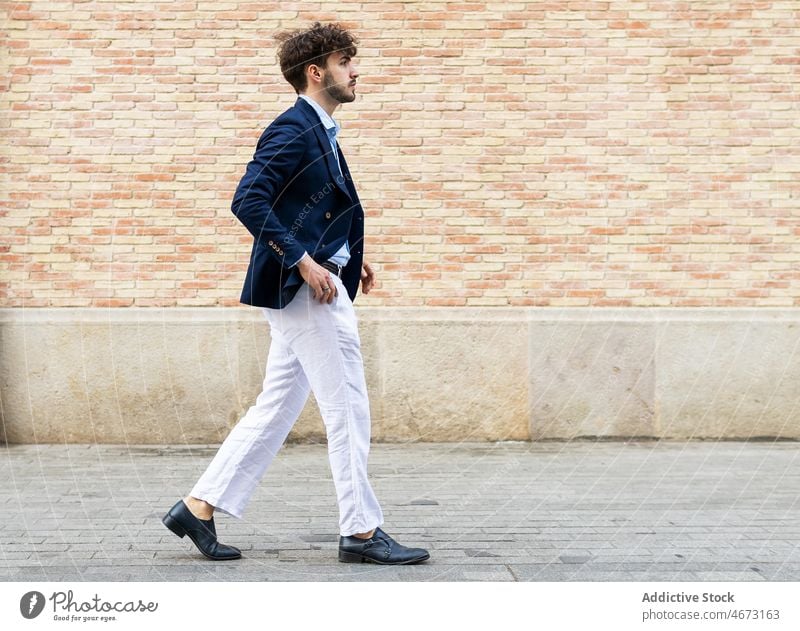 Eleganter hispanischer Mann in der Nähe einer Mauer Stil Großstadt Straße elegant Backsteinwand Anzug Spaziergang formal Vorschein urban schlendern männlich
