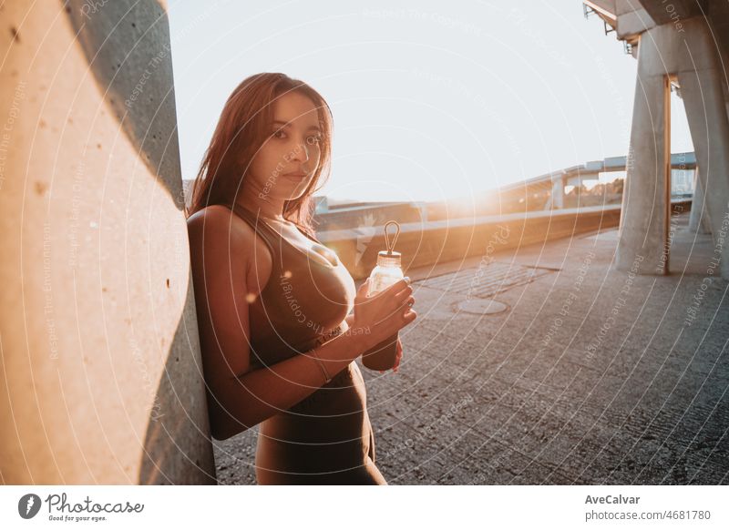 Junge Frau Silhouette ruht gegen eine Wand hält eine Flasche Wasser während einer bunten Sonnenuntergang mit Kopie Raum. Ausruhen nach dem Training auf städtischen Straße ambient Konzept. Marokkanisches Mädchen