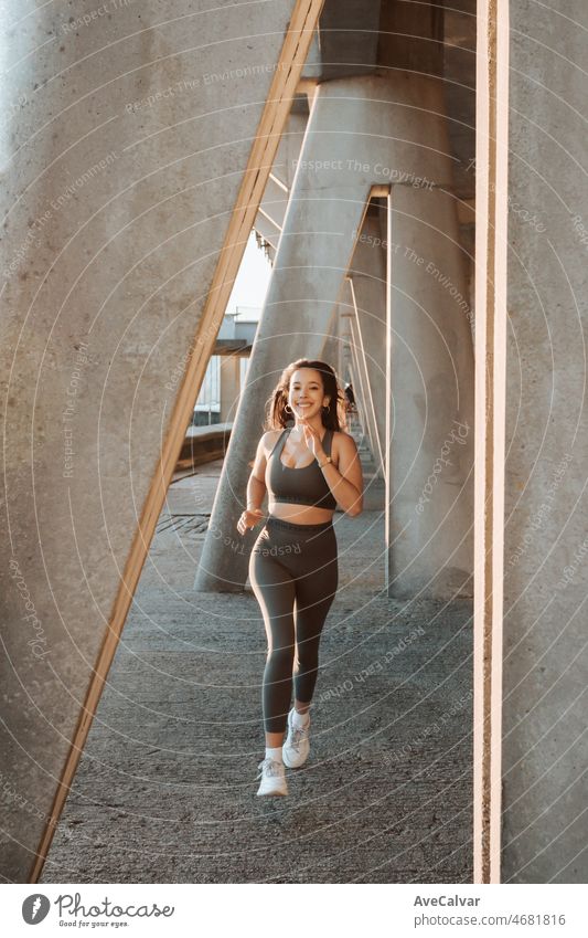 Junge multikulturelle Frau lächelt in die Kamera, während sie in der Stadt joggt, um vor dem Sommer Gewicht zu verlieren und einen definierten Körper zu bekommen. Laufen und Workout im Freien. Sonnenuntergang Szene mit jungen Athleten