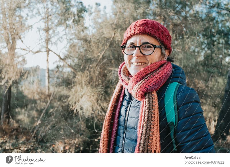Alte Frau in Winterkleidung und Hut lächelnd während eines Tages im Freien. Ältere Menschen Aktivitäten in der Natur während des Sonnenuntergangs. Psychische Gesundheit Großmutter Konzept