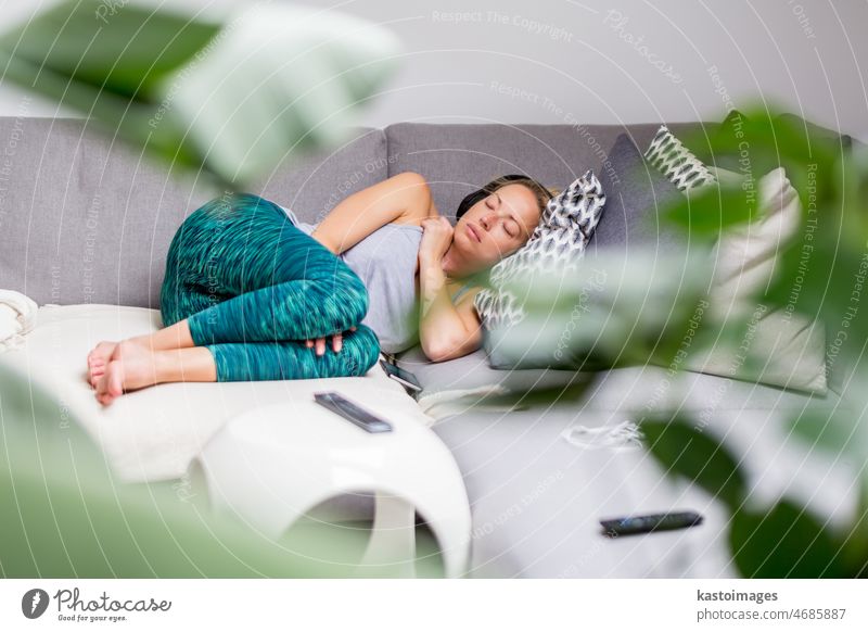 Junge lässige Frau auf Couchkissen liegend mit geschlossenen Augen, entspannend auf gemütlichem Sofakissen, entspanntes Mädchen, das ein Nickerchen zu Hause macht, Kopfhörer tragend, Musik oder Podcast hörend
