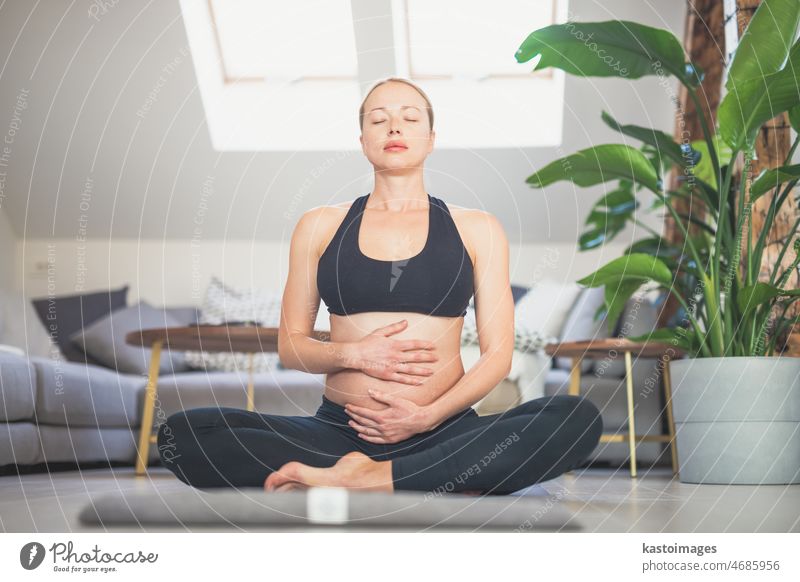 Junge schöne schwangere Frau Ausbildung Yoga, streichelt ihren Bauch. Junge glückliche werdende entspannen, denken über ihr Baby und genießen ihr zukünftiges Leben. Mutterschaft, Schwangerschaft, Yoga-Konzept.