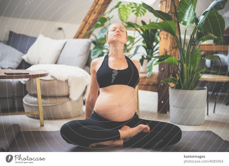 Junge schöne schwangere Frau trainiert Yoga zu Hause in ihrem Wohnzimmer. Mutterschaft, Schwangerschaft, gesunder Lebensstil und Yoga-Konzept Baby Pflege