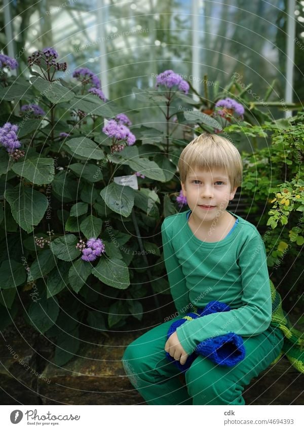 Kindheit | Ausflug in den Botanischen Garten | im Grünen sitzen. Junge blond hellhäutig sitzend Pflanze Blüten Blätter Botanischer Garten Gewächshaus grün lila