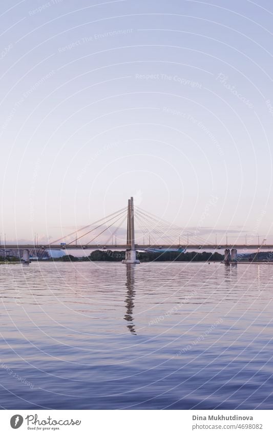Hängebrücke bei Sonnenuntergang zur blauen Stunde. Wolkenloser Himmel, Brücke spiegelt sich im Flusswasser. Städtische Stadtlandschaft und moderne Architektur. Vertikale städtischen Sommer Hintergrund.