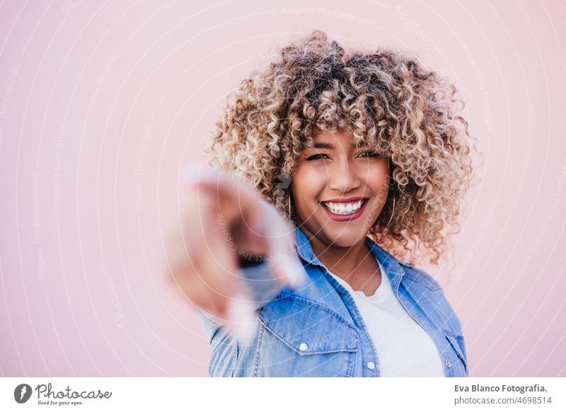 schöne glückliche hispanische Frau mit Afro-Haar im Freien im Frühling mit den Händen zeigen. rosa Hintergrund berühren Afro-Look Glück Lächeln Großstadt