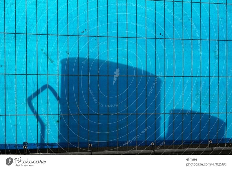Schatten verschiedener Teile hinter einem Metallzaun, der mit einer blauen Kunststoffplane als Sichtschutz bespannt ist / Schattenspiel / Absperrung Plane Zaun