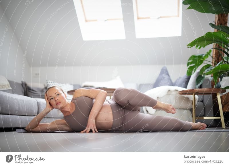 Junge schöne schwangere Frau Training Pilates zu Hause in ihrem Wohnzimmer. Gesunder Lebensstil und aktive Schwangerschaft und Mutterschaft Konzept. Yoga Baby