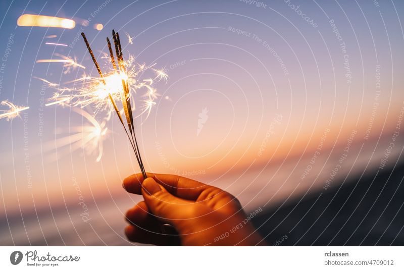 Hand hält Wunderkerze im Sonnenuntergangslicht Strand Feuerwerk Beteiligung Nacht Mädchen Party Menschen Sommer Frau abstrakt Hintergrund brennend Feier Flamme