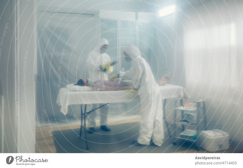 Ärzte in bakteriologischem Schutz bei der medizinischen Untersuchung eines auf einer Trage liegenden Patienten Feldkrankenhaus Isolation Arzt Schutzanzug