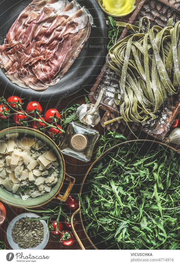 Italienisches Essen Hintergrund mit Parmaschinken, grüne Nudeln, Tomaten, Rucola, Olivenöl, Kräuter Italienische Küche Küchenkräuter Knoblauch Essen zubereiten