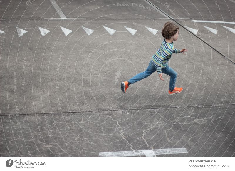 Kind rennt über einen Platz mit Pfeilen rennen Geschwindigkeit schnell Dynamik laufen Bewegung bewegen Kindheit sportlich Sport Spielen urban Stadt Parkplatz