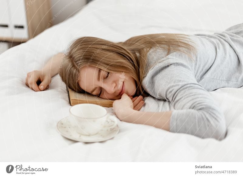 Ein junges Mädchen liegt mit geschlossenen Augen, ein Buch in der Hand, auf dem Bett zu Hause Frau lesen Lügen Schlafzimmer Morgen ruhen grau schön