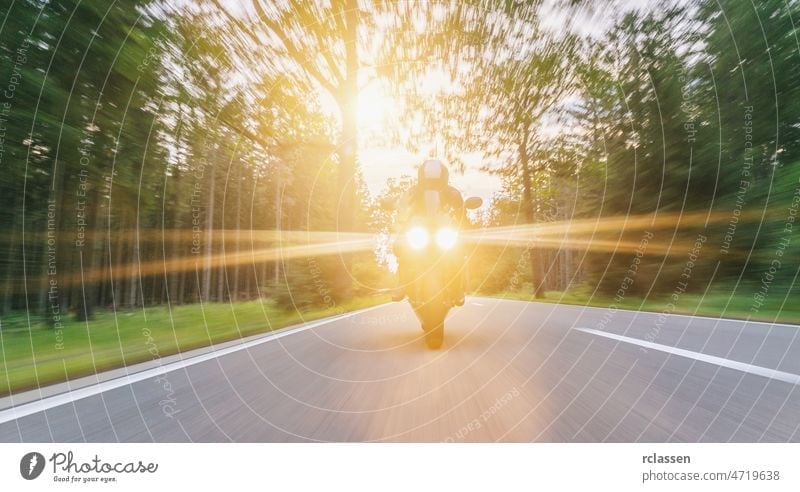 Motorrad auf der Waldstraße mit Scheinwerfern fahrend. Fahren auf der leeren Straße auf einer Motorradtour bei Sonnenuntergang. copyspace für Ihren individuellen Text.