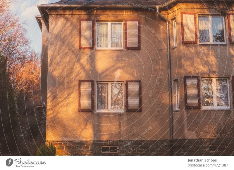 Fassade Altbau Haus mit Fensterläden mit Schatten in Abendlicht Fensterladen Mehrfamilienhaus Eigenheim Stadtrand wohnen alt Miete Bäume warmes Licht abends