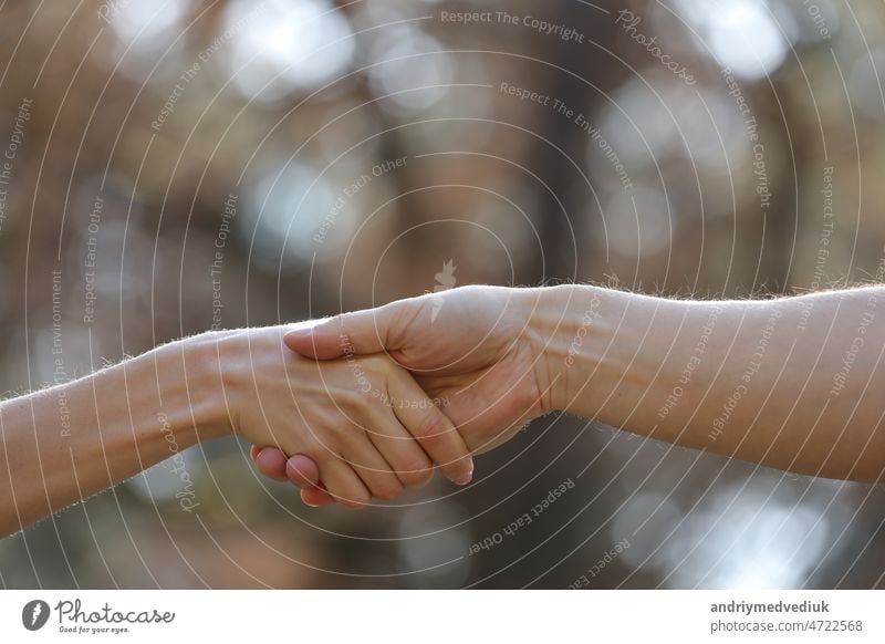 Handshake zwei Menschen auf die Natur Hintergrund. Close Up von weiblichen und männlichen Händedruck. Händchenhalten ist eine Form der körperlichen Intimität zwischen zwei oder mehreren Personen. Es kann romantisch sein, muss es aber nicht.