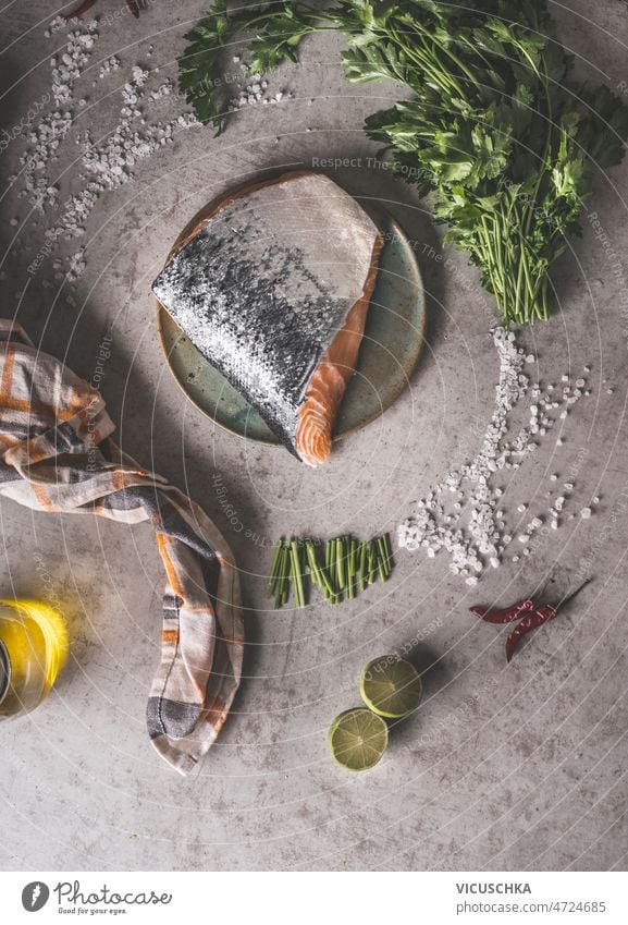 Rohes Lachssteak mit Schuppen am Teller auf grauem Betonküchentisch roh Tisch Salz Petersilie Kalk Olivenöl Küchentuch Gesundheit Essen zubereiten heimwärts