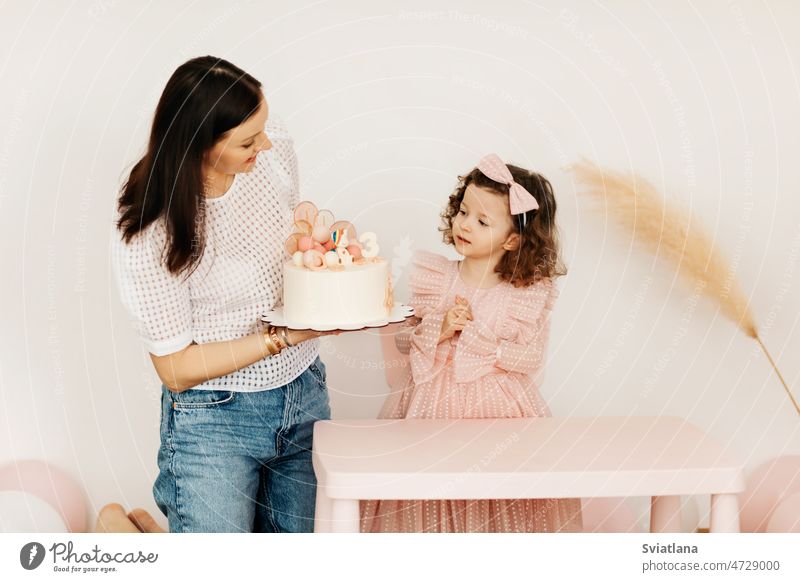 Eine junge Mutter und ihre kleine Tochter feiern ihren Geburtstag mit einer Torte. Kuchen Mama Tisch zu feiern heimwärts wenig Geschenk Partnerschaft schön Kind