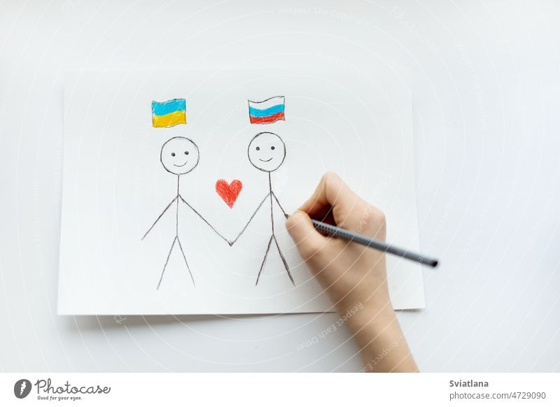 Ein Kind zeichnet auf ein Blatt Papier zwei Kinder mit einer Zeichnung von zwei Flaggen der Ukraine und Russlands in Großaufnahme. Blick von oben. Kinder gegen den Krieg