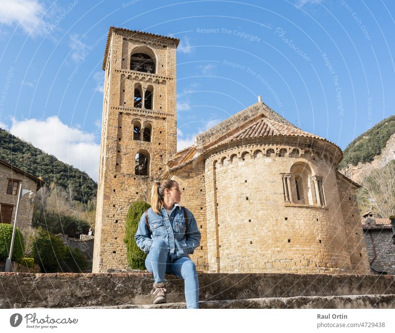 Schöne junge Frau, die in einem schönen mittelalterlichen Dorf sitzt und entspannt Beget besucht, mit der romanischen Kirche von Saint Christopher im Hintergrund