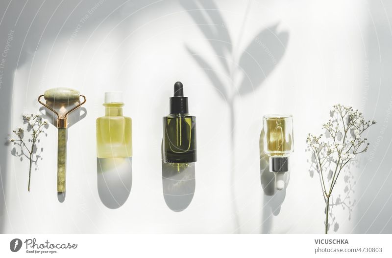 Grüne Schönheitsprodukte mit Blumen auf weißem Hintergrund mit natürlichem Sonnenlicht und Schatten grün weißer Hintergrund Kosmetikflaschen Massageroller