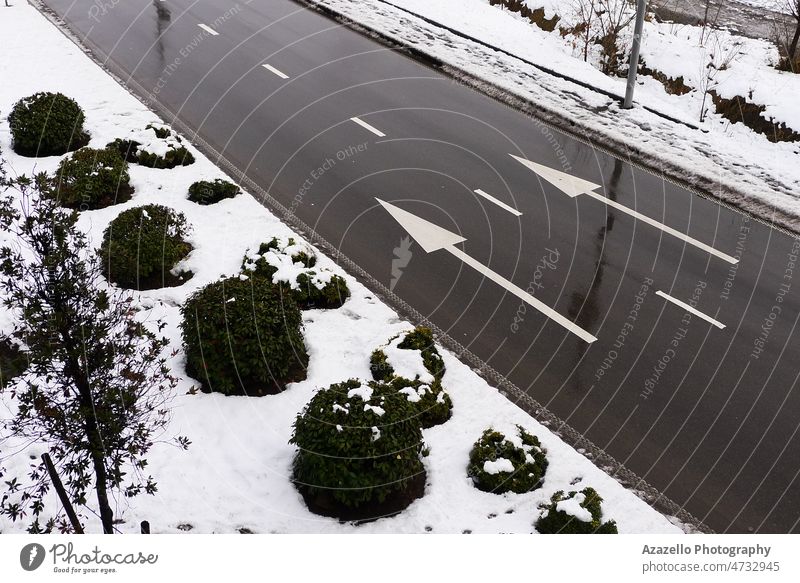 Winterstraße mit zwei parallelen weißen Pfeilen. Weiße Pfeile auf einer nassen Asphaltstraße. abstrakt Kunst Hintergrund Buchse dunkel unbewegliche Design