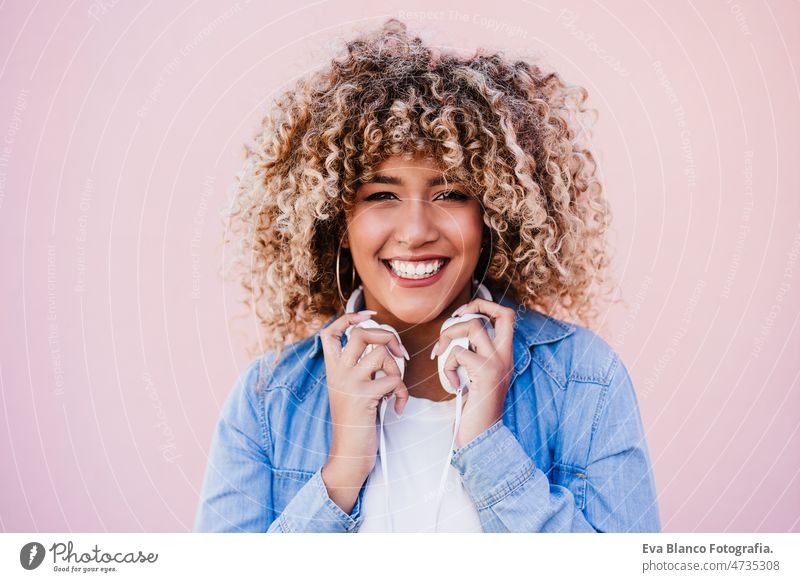 Porträt einer lächelnden hispanischen Frau mit Afro-Haar in der Stadt, die ein Mobiltelefon und ein Headset benutzt. lifestyle hören Körperfreundlichkeit