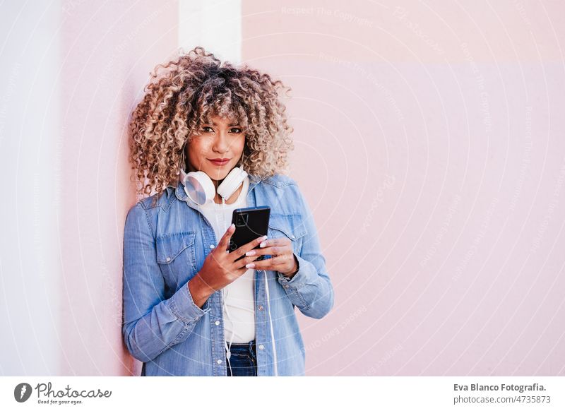 glückliche kurvige hispanische Frau mit Afro-Haar in der Stadt mit Handy und Headset. Körperliche Positivität hören Körperfreundlichkeit kurvenreich Großstadt