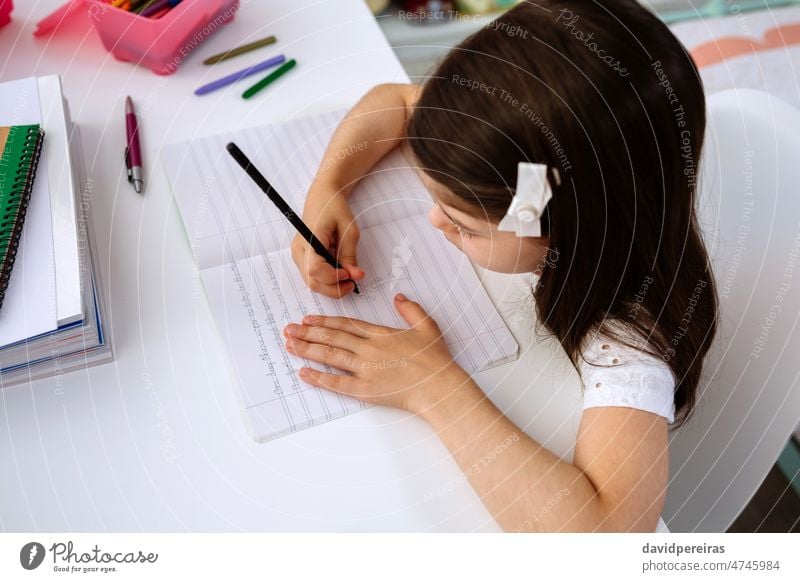Mädchen macht Hausaufgaben am Schreibtisch sitzend verwendet Schule zu Hause Zeichnung Notebook heimwärts Homeschooling schreibend konzentriert niedlich Kind