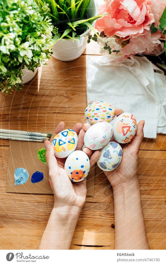 Frau hält ein modernes Osterei. Pinsel und malt mit Blumen und Pflanzen. Glückliche Ostern Konzept auf einem hölzernen Hintergrund. Beteiligung Hand Eier Feier