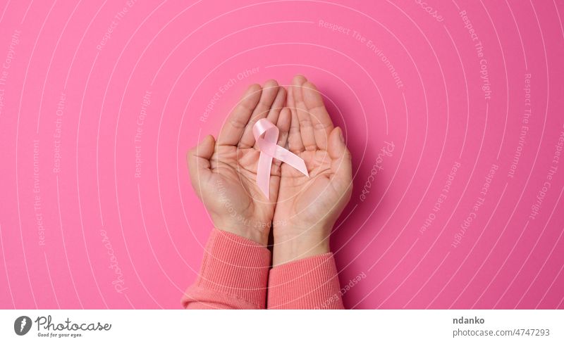 zwei weibliche Hände halten ein rosa Seidenband in Form einer Schleife auf rosa Hintergrund. Symbol für den Kampf gegen Brustkrebs Frau Krankheit Bändchen Hand