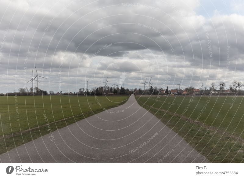 eine asphaltierte Milchstraße die ins Dorf führt Brandenburg Himmel Windkraftanlage Außenaufnahme Menschenleer Wolken dorf brandenburg Tag natur ländlich himmel