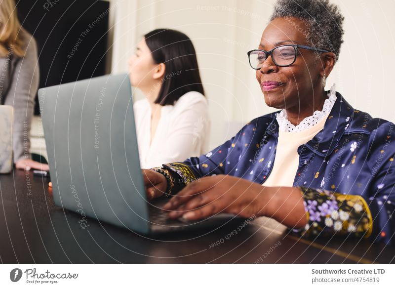 Porträt einer älteren schwarzen Geschäftsfrau mit kurzen grauen Haaren, die eine Brille trägt und einen Laptop benutzt Senior Frau Business Lächeln Glück