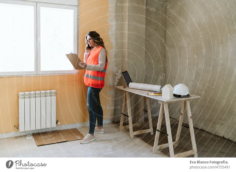 Professionelle Architektin auf einer Baustelle, die mit einem Mobiltelefon spricht und Baupläne hält Frau Blaupausen Arbeitsbereich Schutzhelm Schutzmantel