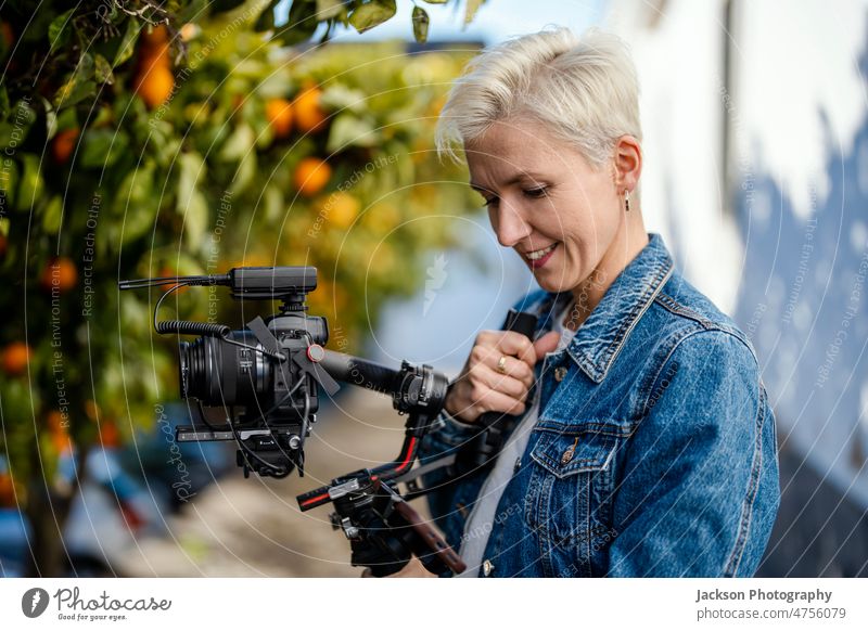 Kameramann mit Filmaufbau im Freien Filmemacher Video Betreiber Frau Gerät Mikrofon Fotokamera orange Orangenbaum Porträt Hipster Verschlussdeckel stabilisiert