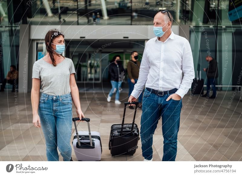 Reisende mit Schutzmasken unterhalten sich beim Verlassen des Flughafens mit ihrem Gepäck reisen Pandemie Mundschutz Frau Mann plaudernd Talkrunde reden Junge