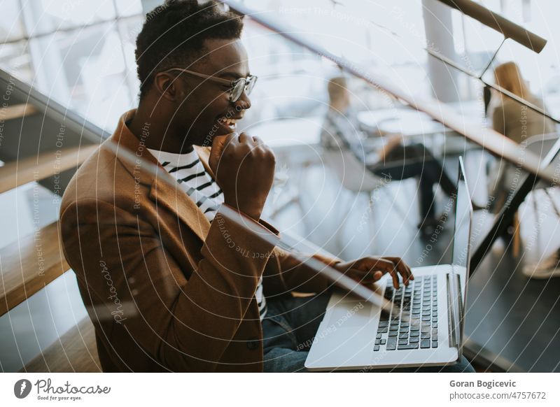 Junger afroamerikanischer Geschäftsmann, der an einem Laptop arbeitet, während er auf einer Bürotreppe sitzt Afrikanisch Amerikaner schwarz Brainstorming