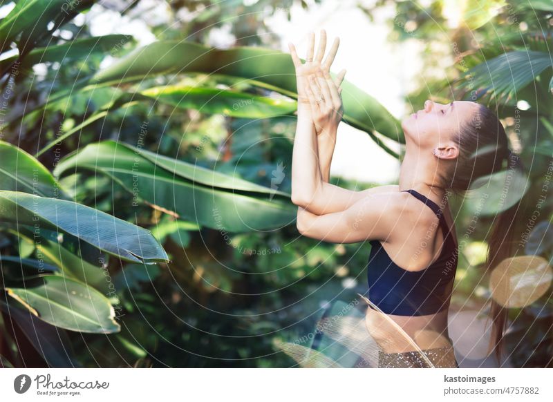 Frau meditiert und praktiziert Yoga im tropischen Regenwald. Schöne junge Frau übt Yoga im Freien mit tropischen Wald im Hintergrund. Rückzug Meditation Person