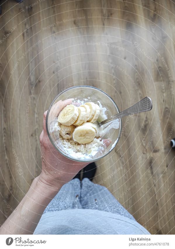Draufsicht auf eine Hand, die einen Brei mit Banane und Joghurt im Glas hält Haferbrei Gesundheit Frühstück Schalen & Schüsseln Hintergrund Diät Frucht Müsli