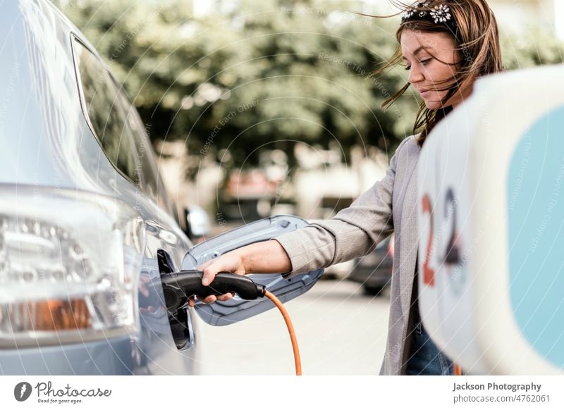 Eine Frau lädt ein Elektroauto in der Stadt auf Steckdose PKW Nahaufnahme Aufladen wiederaufladbar jung urban Ladegerät Ökologie Sauberkeit Gebühr