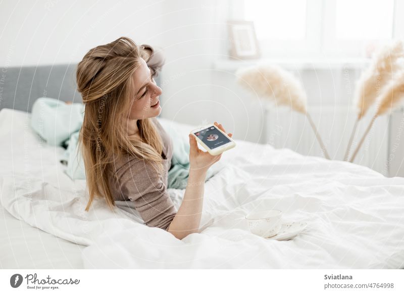 Eine junge Frau telefoniert auf ihrem Smartphone in ihrem gemütlichen Bett. Menschen und Lebensstil Telefon Gespräch Morgen Komfort Lifestyle Top Mobile