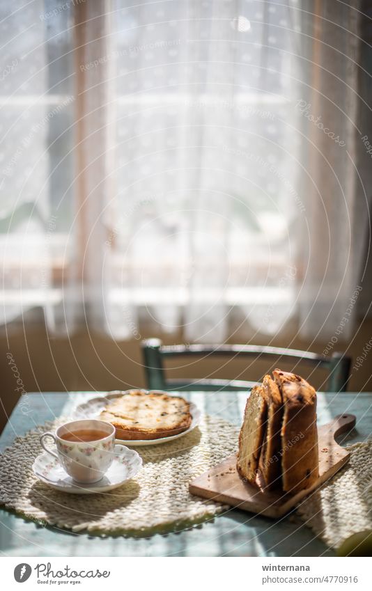 Tisch zu Hause mit einer Tasse Tee und einer Scheibe Osterbrot Vorhänge Licht Morgen heiß warm Scheiben Brot Ostern Stuhl Punkte Fenster Frühling schön Freude