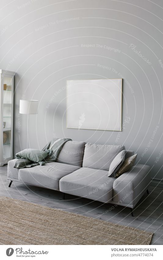 Stilvolle minimalistische Einrichtung des Wohnzimmers in Grau. Sofa mit Plaid, Stehlampe, beige Teppich und Mockup weißen Rahmen an der Wand Liege Möbel grau