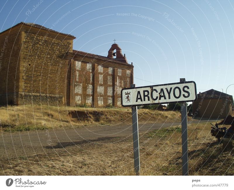 Arcayos Spanien Ausland Süden Friedhof Kirchplatz Straßennamenschild Landstraße Fahrbahn Außenaufnahme rot braun beige Physik Sommer trist Einsamkeit