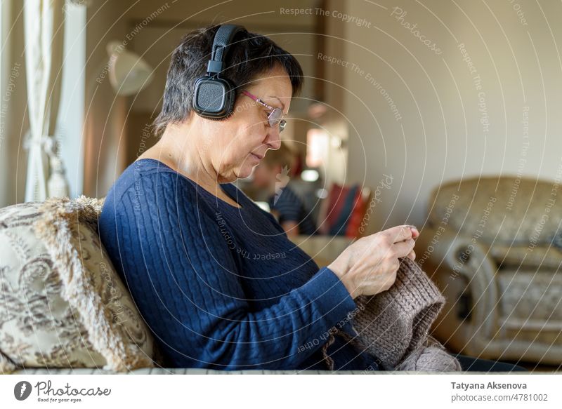 Ältere Frau strickt Hut Senior stricken Hobby Wolle Kopfhörer Musik Erholung handgefertigt reif Nadel Handwerk Sitzen im Innenbereich Person Erwachsener Textil